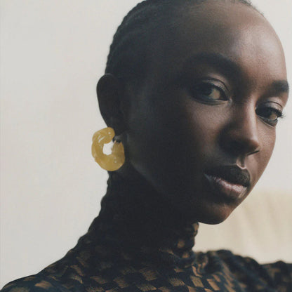 CULT STATEMENTPIECES BLUE BIO RESIN GOLD VERMEIL EARRINGS featuring a clean chic hoop design and modern jelly green color ,perfect for dailylife/party/office/casual occasion. Displayed in a cool  lifestyle setting with a black skin model wearing a black pants.