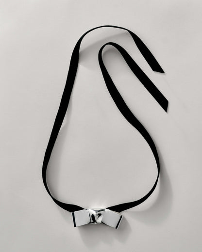 BOW FAUX SUEDE RIBBON CRAVAT NECKLACE featuring a clean chic design and modern nature silver and black color ,perfect for dailylife/party/office/casual occasion. Styled against a white background.