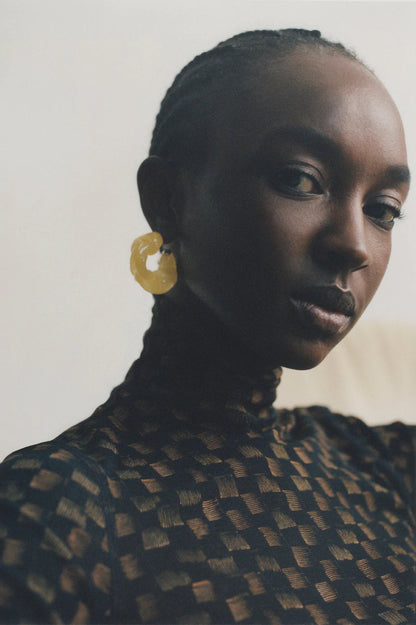 CULT STATEMENTPIECES BLUE BIO RESIN GOLD VERMEIL EARRINGS featuring a clean chic hoop design and modern jelly green color ,perfect for dailylife/party/office/casual occasion. Displayed in a cool  lifestyle setting with a black skin model wearing a black pants.